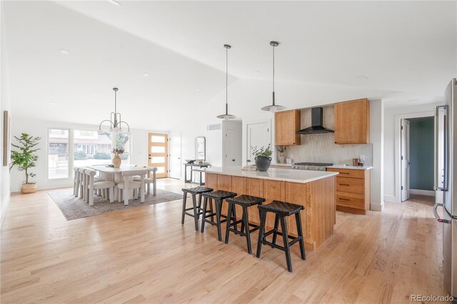 kitchen with stainless steel fridge, hanging light fixtures, wall chimney exhaust hood, light wood-type flooring, and a spacious island