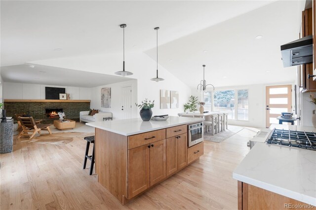 kitchen featuring a brick fireplace, decorative light fixtures, a spacious island, and light wood-type flooring