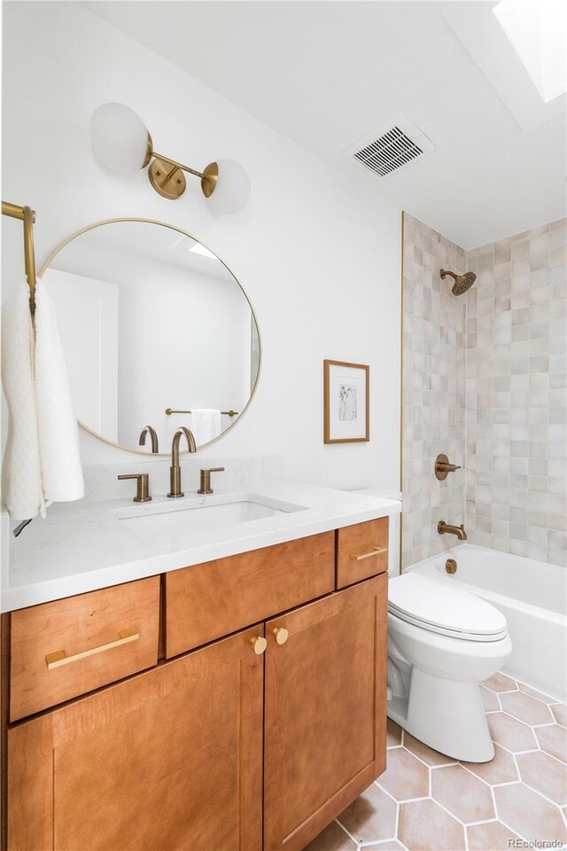 full bathroom featuring a skylight, vanity, tile patterned floors, toilet, and tiled shower / bath