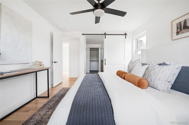 bedroom featuring ceiling fan, a barn door, and light hardwood / wood-style flooring