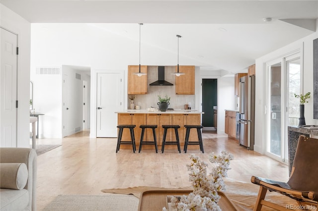 kitchen with high quality fridge, pendant lighting, a breakfast bar area, backsplash, and wall chimney range hood