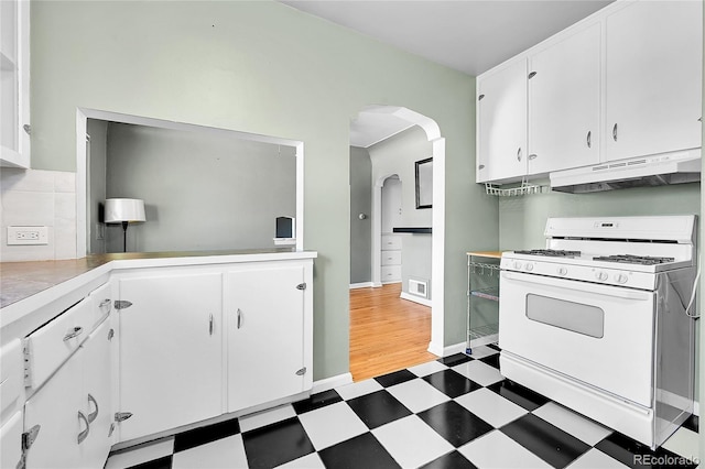 kitchen with white range with gas cooktop, under cabinet range hood, light flooring, arched walkways, and white cabinetry
