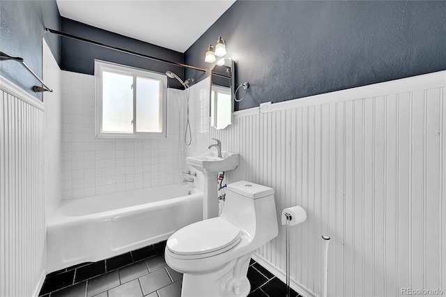 bathroom with toilet, tile patterned floors, bathing tub / shower combination, a wainscoted wall, and a textured wall