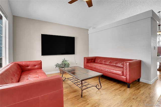 living room with ceiling fan, a textured ceiling, baseboards, and wood finished floors