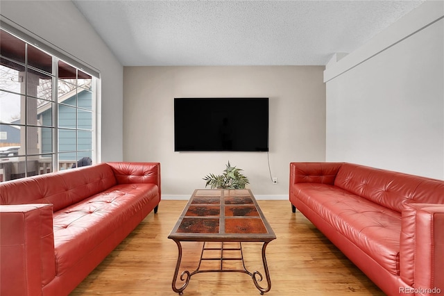 living room with light wood-type flooring, baseboards, and a textured ceiling