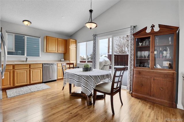 dining space featuring vaulted ceiling, light wood finished floors, and a textured ceiling