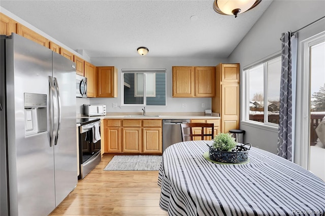 kitchen featuring light wood finished floors, light countertops, light brown cabinetry, appliances with stainless steel finishes, and a sink