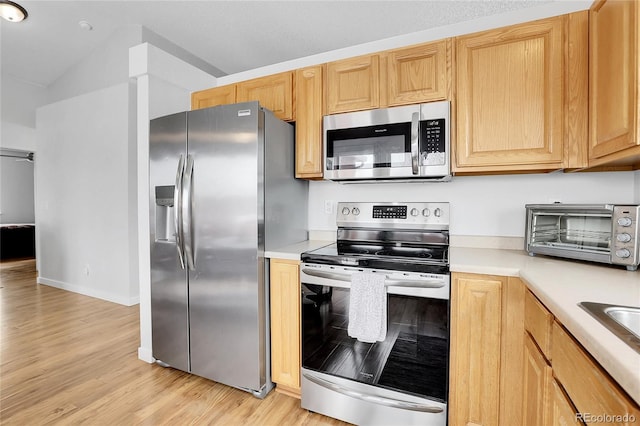 kitchen with a toaster, appliances with stainless steel finishes, light countertops, light brown cabinetry, and light wood-style floors