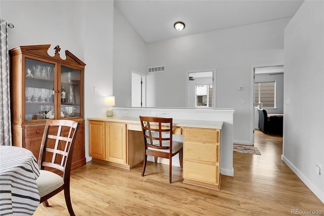 interior space featuring light wood-style flooring, a high ceiling, visible vents, baseboards, and built in study area