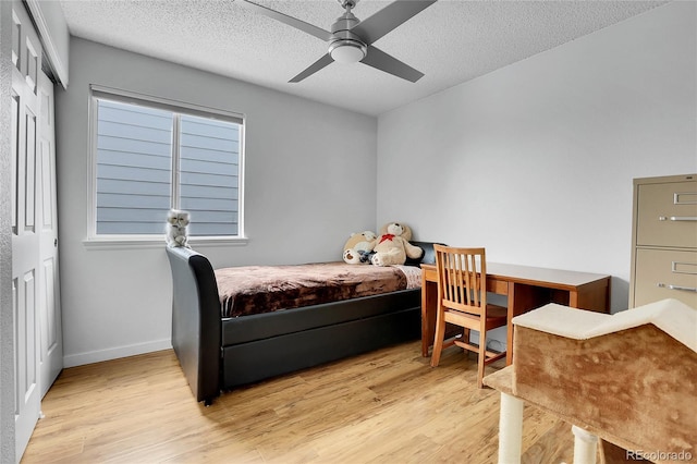 bedroom featuring light wood finished floors, baseboards, a ceiling fan, a textured ceiling, and a closet