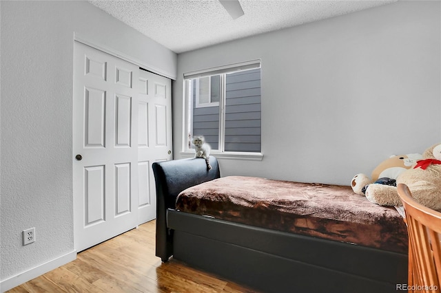 bedroom featuring a textured ceiling, light wood-style flooring, a ceiling fan, baseboards, and a closet