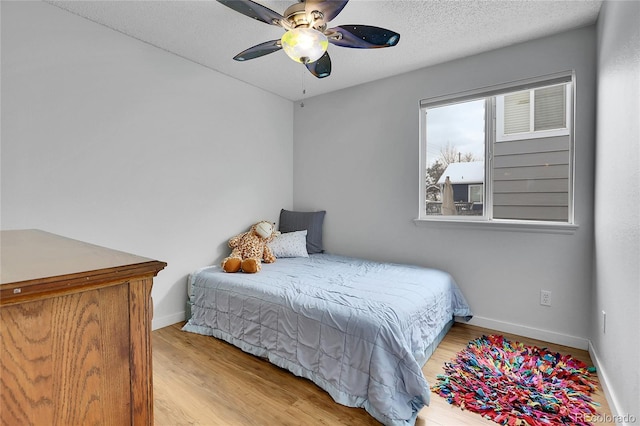 bedroom featuring light wood-style floors, a textured ceiling, baseboards, and a ceiling fan