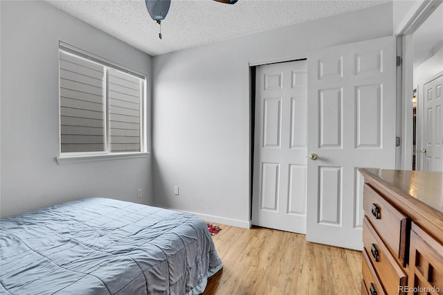 bedroom featuring light wood finished floors, multiple windows, baseboards, and a textured ceiling