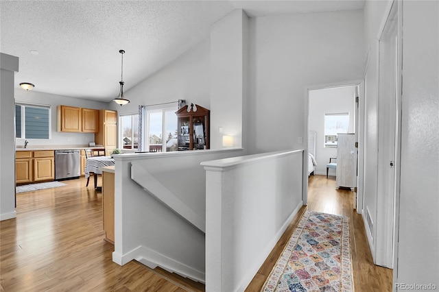 hall featuring a textured ceiling, light wood-type flooring, a sink, and an upstairs landing