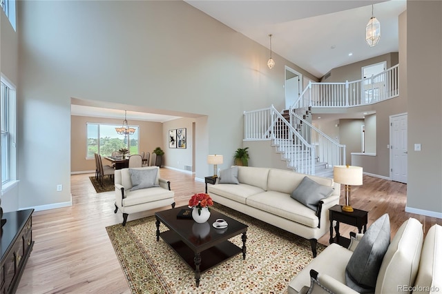 living room with a towering ceiling, light hardwood / wood-style flooring, and an inviting chandelier