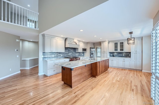 kitchen featuring an island with sink, hanging light fixtures, light hardwood / wood-style flooring, light stone countertops, and tasteful backsplash