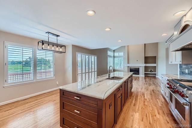 kitchen with hanging light fixtures, light stone countertops, light hardwood / wood-style flooring, sink, and double oven range