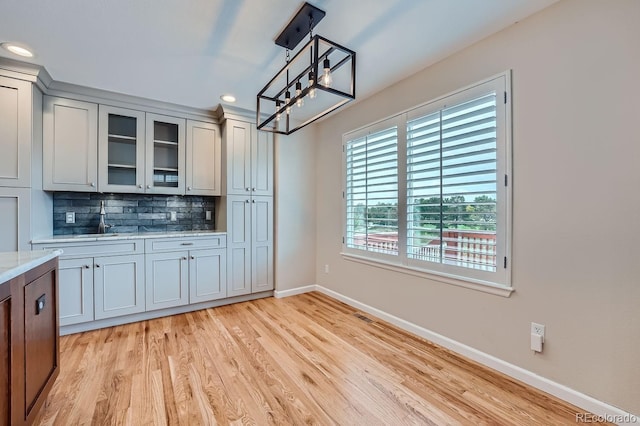 kitchen featuring light hardwood / wood-style floors, decorative backsplash, light stone counters, and hanging light fixtures