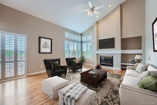 living room featuring light hardwood / wood-style flooring, a tiled fireplace, high vaulted ceiling, and plenty of natural light