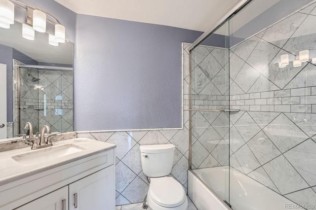 full bathroom with tile walls, vanity, bath / shower combo with glass door, and toilet