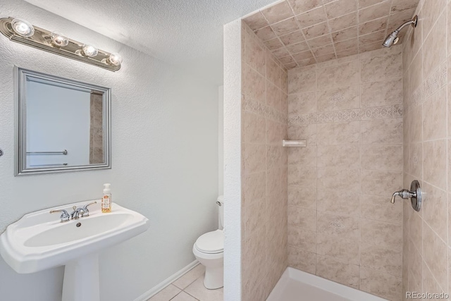 bathroom featuring tile patterned floors, toilet, sink, a tile shower, and a textured ceiling