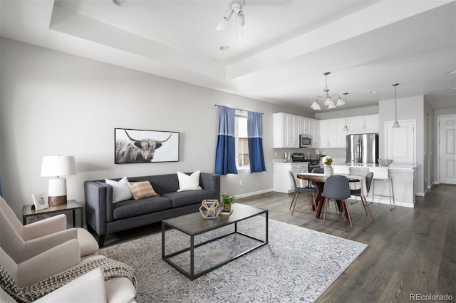 living room with a tray ceiling, dark wood-style flooring, ceiling fan, and baseboards