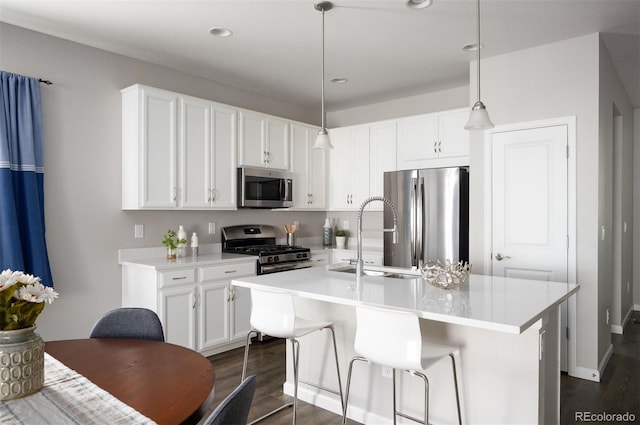 kitchen with an island with sink, hanging light fixtures, stainless steel appliances, light countertops, and white cabinetry