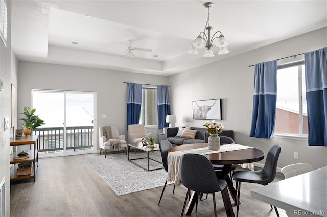 dining space featuring ceiling fan with notable chandelier, wood finished floors, a raised ceiling, and baseboards