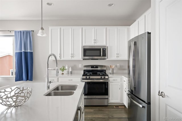 kitchen featuring stainless steel appliances, light countertops, hanging light fixtures, white cabinets, and a sink