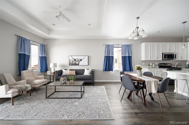 living room with dark wood-style floors, baseboards, a raised ceiling, and ceiling fan with notable chandelier