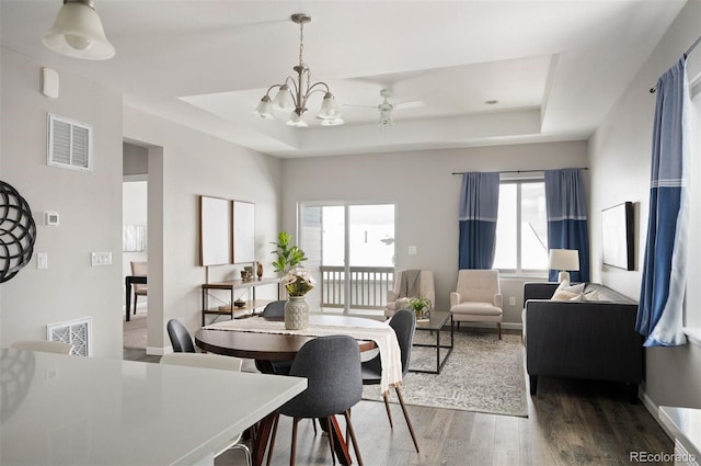 dining space with a tray ceiling, dark wood-style flooring, visible vents, and baseboards