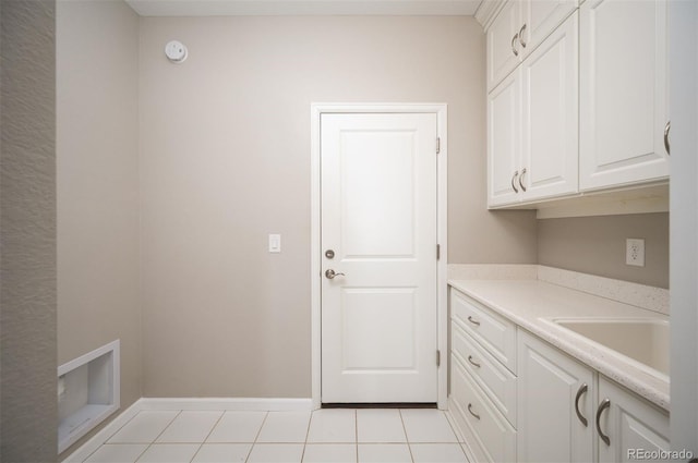 laundry room with baseboards, light tile patterned flooring, cabinet space, and a sink