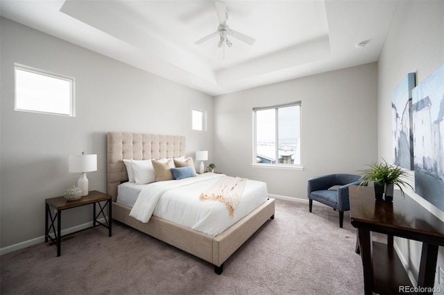 carpeted bedroom with a raised ceiling, a ceiling fan, and baseboards