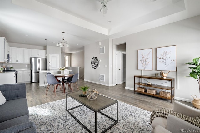 living area with light wood-style floors, a chandelier, baseboards, and a raised ceiling