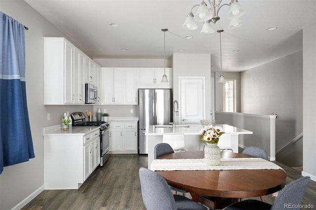 kitchen with stainless steel appliances, an island with sink, baseboards, a chandelier, and dark wood finished floors