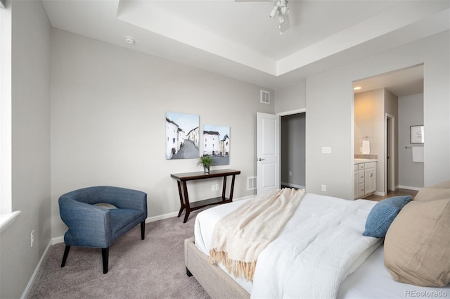 bedroom with light colored carpet, baseboards, a tray ceiling, and ensuite bath
