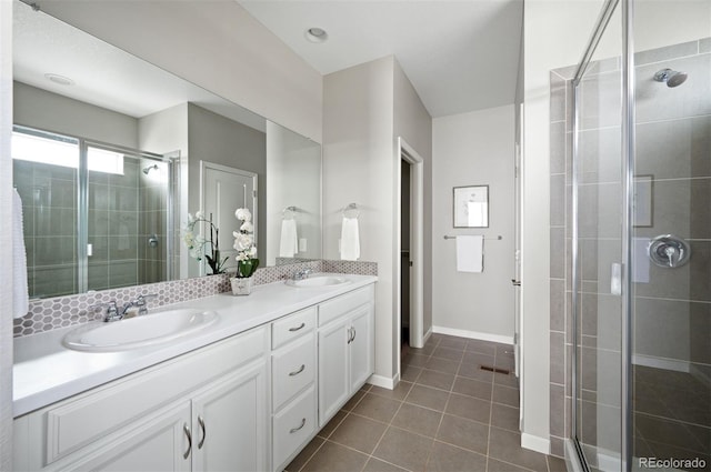 bathroom featuring a stall shower, double vanity, tile patterned flooring, and baseboards