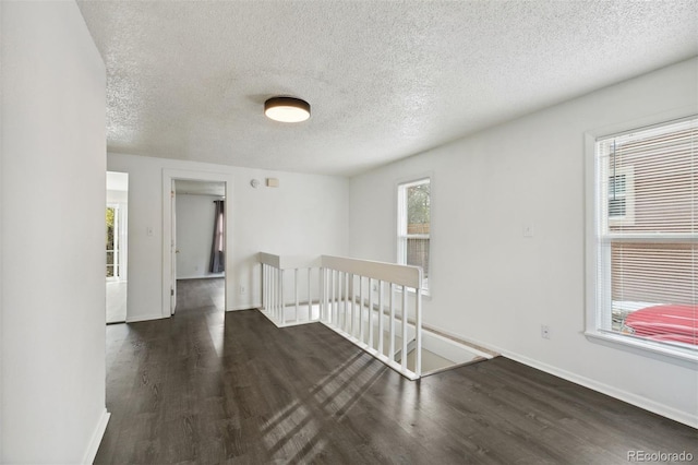 unfurnished room with a textured ceiling, plenty of natural light, and dark hardwood / wood-style floors