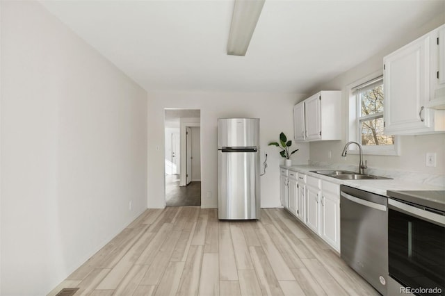 kitchen with white cabinets, appliances with stainless steel finishes, light hardwood / wood-style flooring, and sink