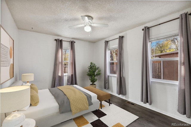 bedroom featuring a textured ceiling, multiple windows, dark wood-type flooring, and ceiling fan