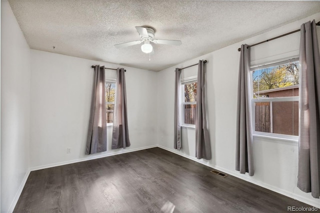 empty room with a wealth of natural light, ceiling fan, dark wood-type flooring, and a textured ceiling