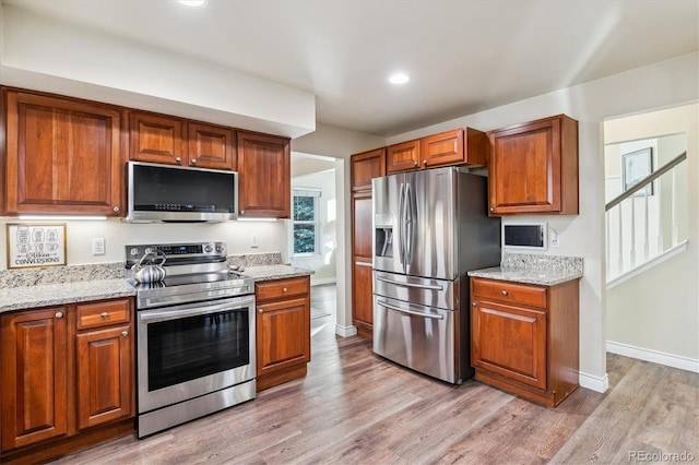 kitchen with appliances with stainless steel finishes, light stone countertops, and light hardwood / wood-style floors