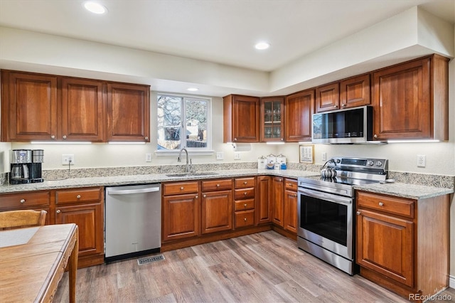 kitchen with light stone counters, appliances with stainless steel finishes, sink, and light wood-type flooring