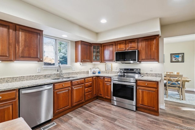 kitchen featuring light stone counters, appliances with stainless steel finishes, light hardwood / wood-style floors, and sink