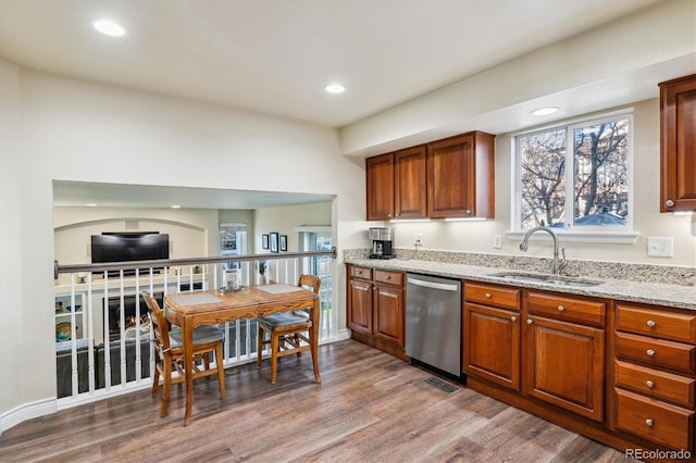 kitchen featuring hardwood / wood-style floors, light stone countertops, sink, and stainless steel dishwasher