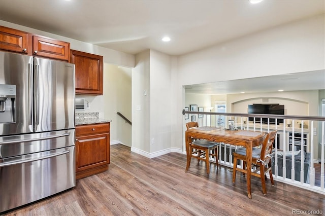 kitchen with stainless steel refrigerator with ice dispenser, light stone countertops, and wood-type flooring