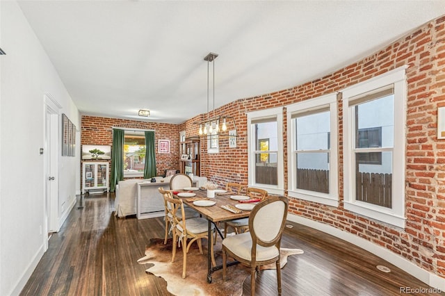 dining area with dark hardwood / wood-style flooring, brick wall, and a notable chandelier