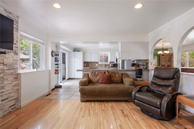 living area with crown molding, arched walkways, an inviting chandelier, and light wood-style floors
