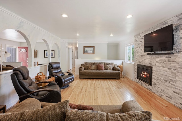 living area featuring crown molding, arched walkways, a stone fireplace, hardwood / wood-style floors, and recessed lighting