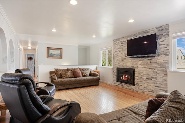 living room with ornamental molding, wood finished floors, a stone fireplace, baseboards, and recessed lighting